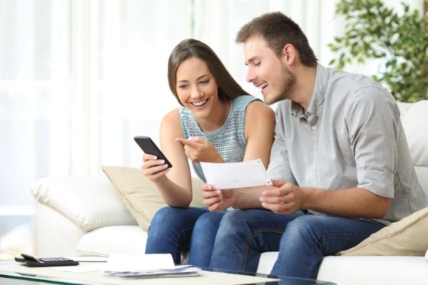 smiling couple sitting looking at cell phone, man holding a piece of paper.
