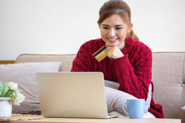 A young Asian woman with a happy smile holds a credit card and uses a smartphone to shop online Online payment concept.